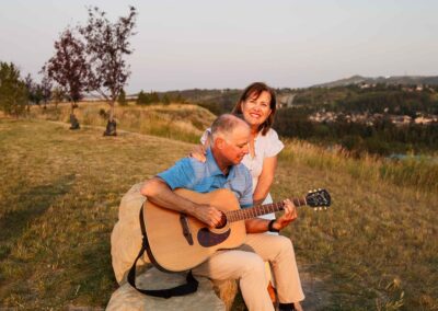 man sitting on a rock playing guitar by his wife