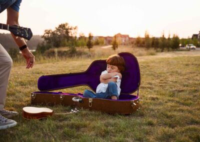 Toddler sitting inside an open guitar case in a field