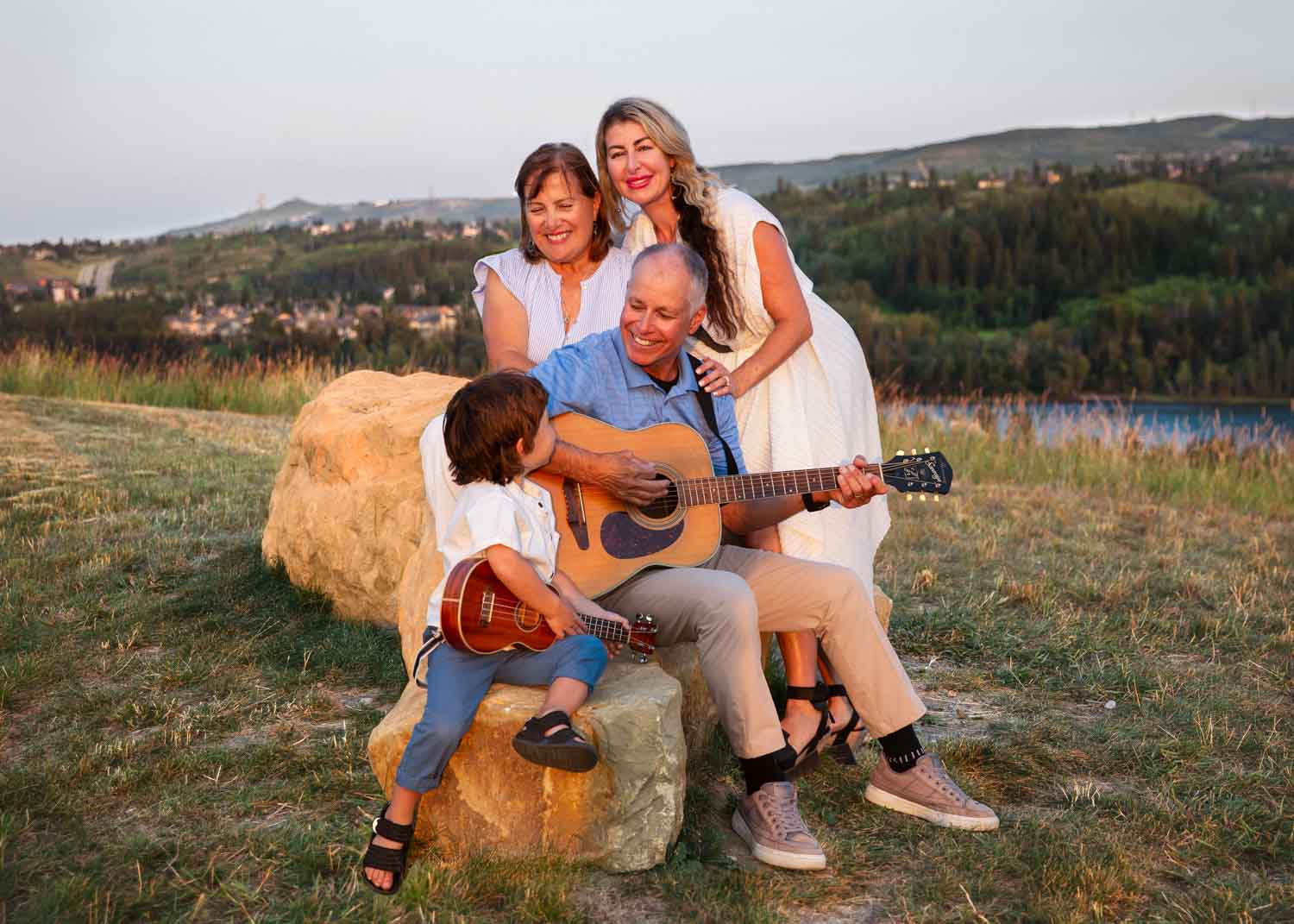 Family of four gathered around guitar and ukulele on a large rock