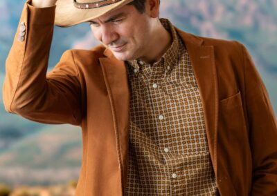 Man in a cowboy hat and brown jacket standing against mountains